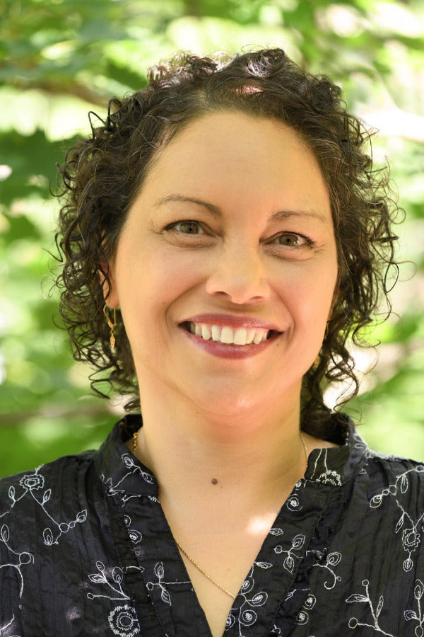 Woman with curly hair smiling outdoors with greenery in the background