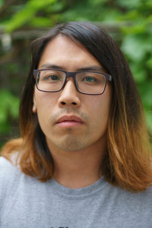 Person with glasses and long hair against a green leafy background