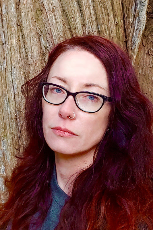 Woman with glasses and red hair standing against a wooden background