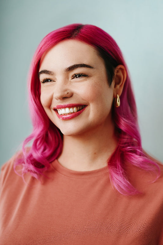 Person with pink hair and a nose ring smiling against a plain background